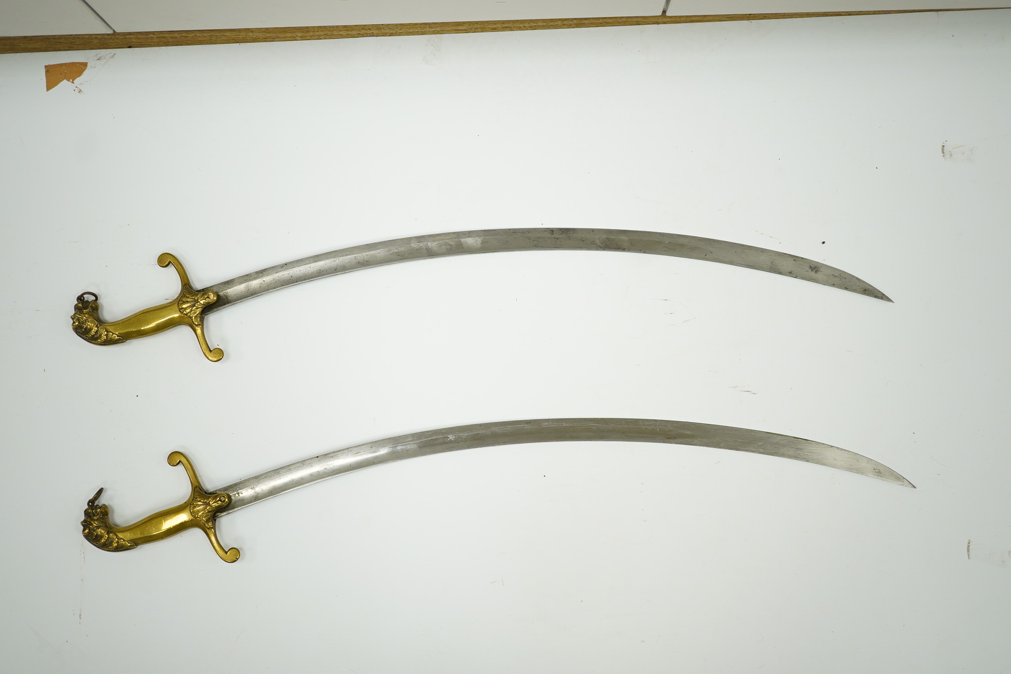 A pair of Victorian bandsman’s swords of Shamshir type, curved single edge blades, cast brass hilts with lions head pommels, in their brass scabbards. Condition - good, some dents to scabbards.